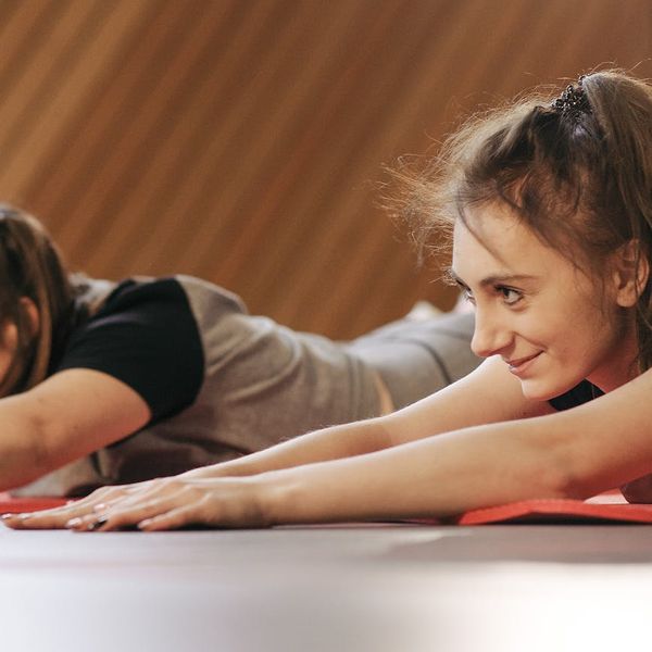 Smiling woman stretching gently on a yoga mat in a bright studio.